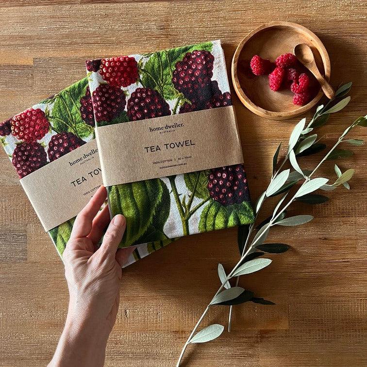 Cotton art tea towel with berries botanical design folded on kitchen bench