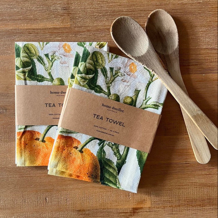 cotton art tea towel with vintage botanical design folded on kitchen bench with wooden utensils