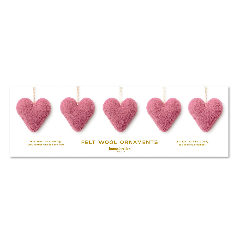 A white rectangular card displaying five pink felt wool heart ornaments hanging by thin strings, with gold text reading 'FELT WOOL ORNAMENTS' and small descriptive copy on a white background.