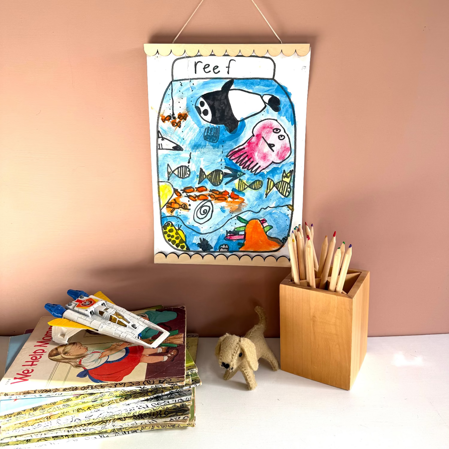 Children's drawing of a fish tank hanging on a wall with books and a toy below.