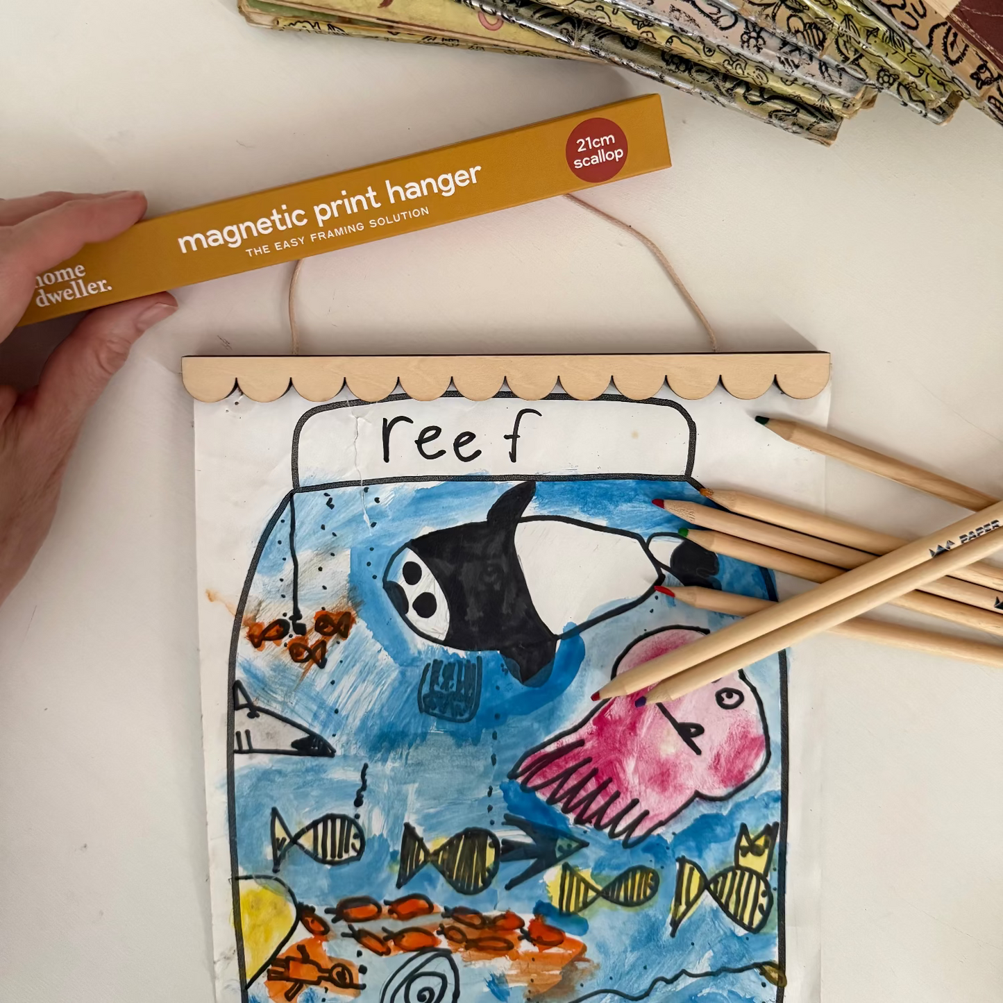 Colorful artwork of a fish scene with a magnetic print hanger and pencils on a white surface.